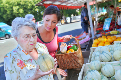 young woman helping elderly woman buying vegetables and fruits in the market